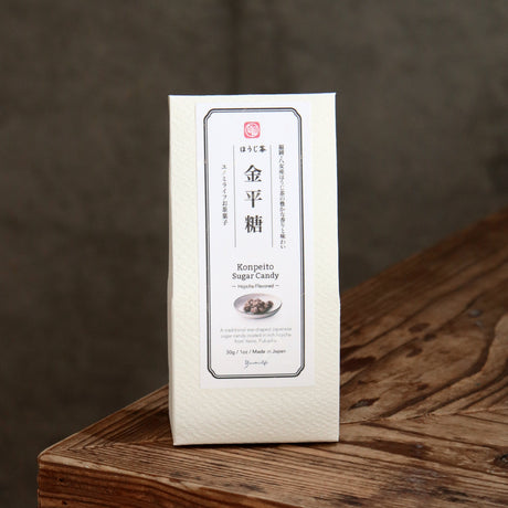 A white rectangular package of Japanese konpeito sugar candy stands upright on a rustic wooden surface against a dark gray background.