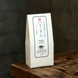 A white paper bag of Snowball Cookies stands upright on a rustic wooden surface against a dark, blurred background.